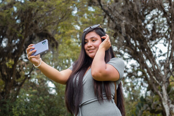 Mujer joven y atractiva sentada en un parque de otoño, sosteniendo su teléfono móvil en las manos, retrato de perfil de una adorable mujer,selfie,celular,