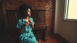 © skyNext - View of a ravishing young Brazilian female with curly afro hair sitting on the chair in the room and pensively looking outside the window with a piano behind her and a copy space place on the right