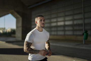 Wall Mural - Strong muscular European guy with cool tattoos jogging on a road