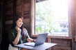 © Thinapob - Happy successful business of asian freelance people business female expressed confidence embolden working with laptop computer sitting with coffee cup beside the window of a wooden house background