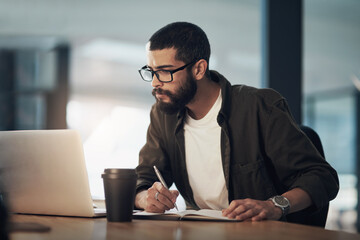 Poster - Every success story is created with hard work. Shot of a young businessman writing in a notebook and using a laptop during a late night in a modern office.