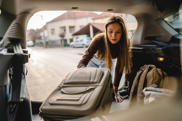 One young beautiful woman student travel concept female take luggage baggage suitcase and other stuff and belongings from the back of her car while moving into dormitory on college campus real people