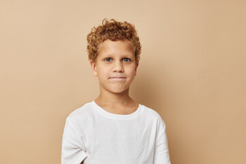 Wall Mural - Cheerful boy with curly hair in a white t-shirt beige background