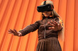 © Sergio Mena - Joven mujer afroamericana usando gafas de realidad virtual en un fondo naranja