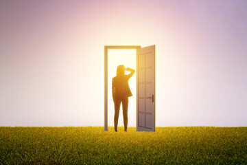 Poster - Successful business woman standing in front of bright door in abstract interior with concrete wall, grass lawn floor. Future, success and dream concept.