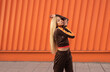 © Sergio Mena - Una alegre mujer afroamericana con ropa deportiva bailando en la calle sobre un fondo naranja