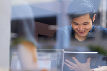 Relaxing in the internet cafe. Smiling Asian man using a digital tablet indoors.