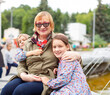 © DariaTrofimova - Old woman hugging  granddaughters at fountain in   park