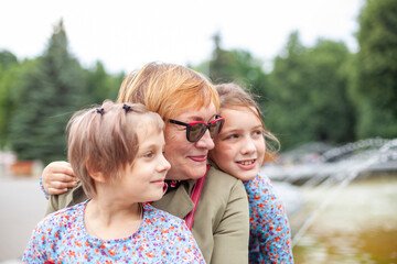 Sticker - Old woman hugging  granddaughters at fountain in   park