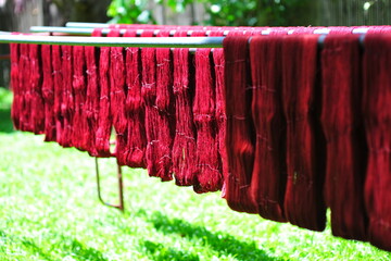 Handmade Thai silk traditional dye process with natural red colour hung on the wooden rail to dry during sunny day. Background is green landscape.