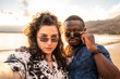 © neonshot - Multiracial fashionable couple, young friends taking selfie , having fun together on the beach. Multi ethnic friendship concept. Honeymoon. Summer time. Traveler.
