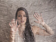 
Medium photo of beautiful brunette young woman seemingly captive looking through sheer material with startled expression