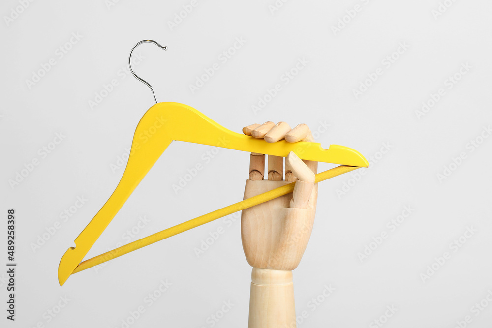 Clothes hanger with wooden mannequin hand on light background