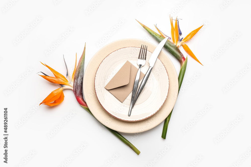 Simple table setting with bird of paradise flowers and envelope on white background