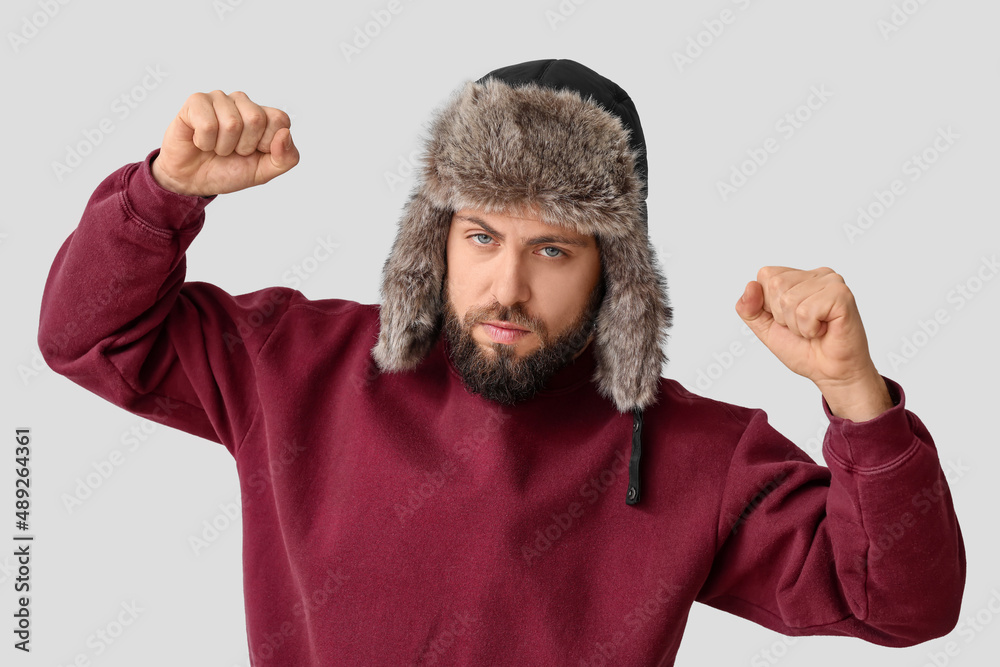 Stylish bearded man in sweater and ear-flapped hat on light background