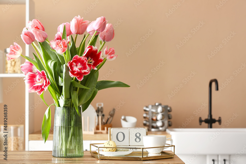 Beautiful tulips, tray with macarons, cup and cube calendar with date 8 MARCH on table in kitchen. International Women's Day celebration