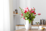 Fototapeta Tulipany - Jug with flowers, cup of coffee and macarons on table in light kitchen