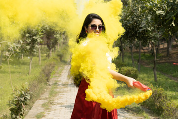 Yellow Smoke bombs color cloud of dry color Holi powder colour gulal abeer with Beautiful young girl woman in spring break in the park Holi festival of color