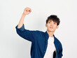 Portrait of handsome Chinese young man with curly black hair in blue shirt posing against white wall background. Fist up in air and looking at camera, looks confident, front view.