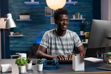 Poster - Smiling freelancer man browsing information on internet working at business project. African american businessman sitting at desk table analyzing financial graphs on computer. Remote work