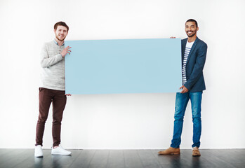 Poster - My mate and I have a message for you. Studio shot of two young men holding a blank placard against a white background.