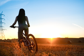 Poster - A girl cycling on the empty field during the sunset. Recreational touristic cycling.