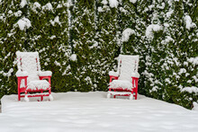 Red Lawn Chairs Covered In Snow On A Patio