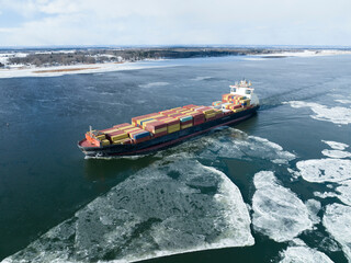 Aerial view of a container ship going upstream through winter ice in the St. Lawrence River near the port of Montreal in Canada