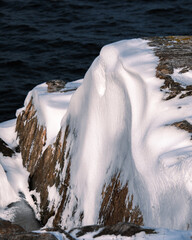 Sticker - A vertical shot of a rocky shore covered in the snow surrounded by the sea under the sunlight