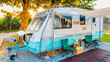 © JinnaritT - Camping chairs placed outside cozy retro travel trailer Caravan under tree before sunset near the river in peaceful countryside. Outdoor and Recreational Vehicles Theme. Travel Industry.