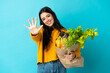 © luismolinero - Young woman holding a grocery shopping bag isolated on blue background counting five with fingers