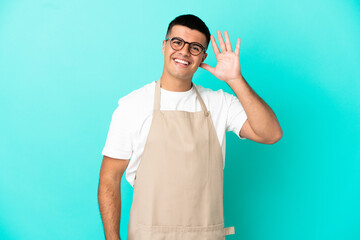 Poster - Restaurant waiter man over isolated blue background listening to something by putting hand on the ear