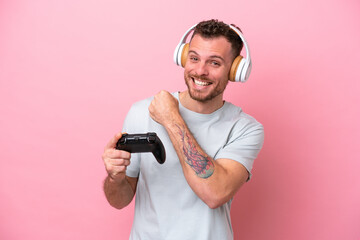 Wall Mural - Young Brazilian man playing with video game controller isolated on pink background celebrating a victory