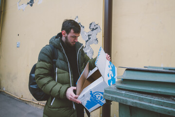 A young man throws a cardboard box into a trash can on the street. Eco-friendly waste collection and separation.