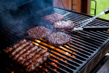 Smoky Hamburger Meat Grilling For Burgers. Fry On An Open Fire On The Grill - Bbq.Burgers And Sausages Cooking Over Flames On The Grill.