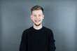 © Alexander - Portrait von einem jungen freundlichen Mann auf grauem Hintergrund lächelnd