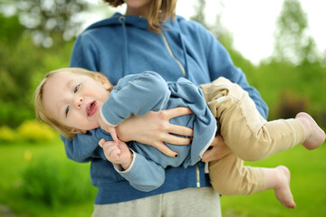 Sticker - Cute funny toddler boy in his mothers arms. Mom and son having fun on sunny summer day in a park. Adorable son being held by mommy.