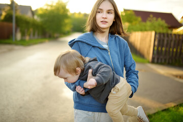 Poster - Cute big sister cuddling with her toddler brother. Adorable teenage girl holding baby boy. Children with large age gap. Big age difference between siblings.