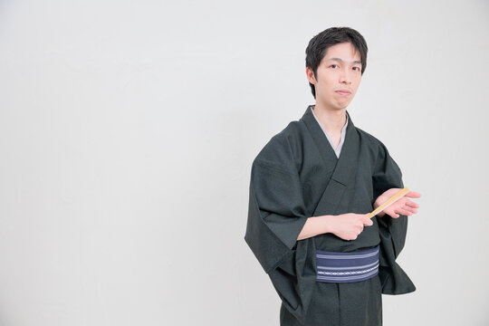 扇子を持って手に当てる着物を着た日本人男性