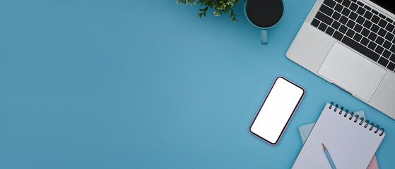 Fototapete - Smart phone, laptop computer, coffee cup and notebook on blue background with copy space.