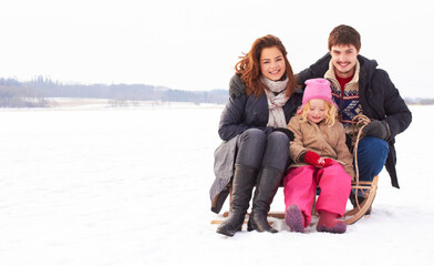  Bonding time on the ice. Two adolescents and a child sitting on a snow sled outdoors on a crisp winters day.