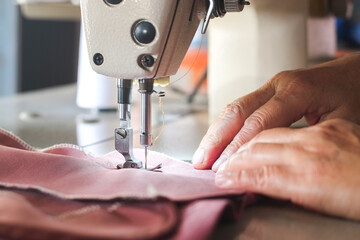 Wall Mural - Hand of seamstress using industrial sewing machine to sew the seams of pink cloth close-up.