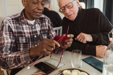Elderly Man Knitting By Male Friend At Retirement Home