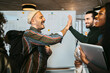 © Maskot - Cheerful male friends giving high-five by woman laughing in college