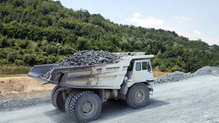 white Haul truck truck load of gravel rocks in the quarry from side view, big and large articulated dumping truck, dumper trailer, dump lorry. off-highway heavy-duty construction.