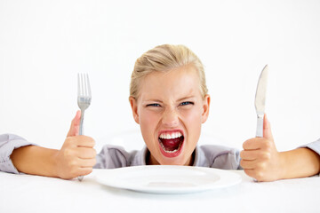 Wall Mural - This is ridiculous Im starving. Furious young woman sitting in front of an empty plate while holding her knife and fork.