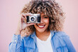© Eva - beautiful happy hispanic woman with afro hair holding vintage camera. pink background