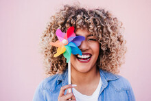 Beautiful Happy Hispanic Woman With Afro Hair Holding Colorful Pinwheel. Pink Background,wind Energy