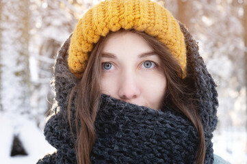 Wall Mural - portrait of a smiling young caucasian woman in a bright woolen hat and scarf, against the backdrop of a snowy forest.