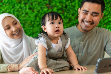 Poster - Young malay couple with toddler at the restaurant smiling to each other